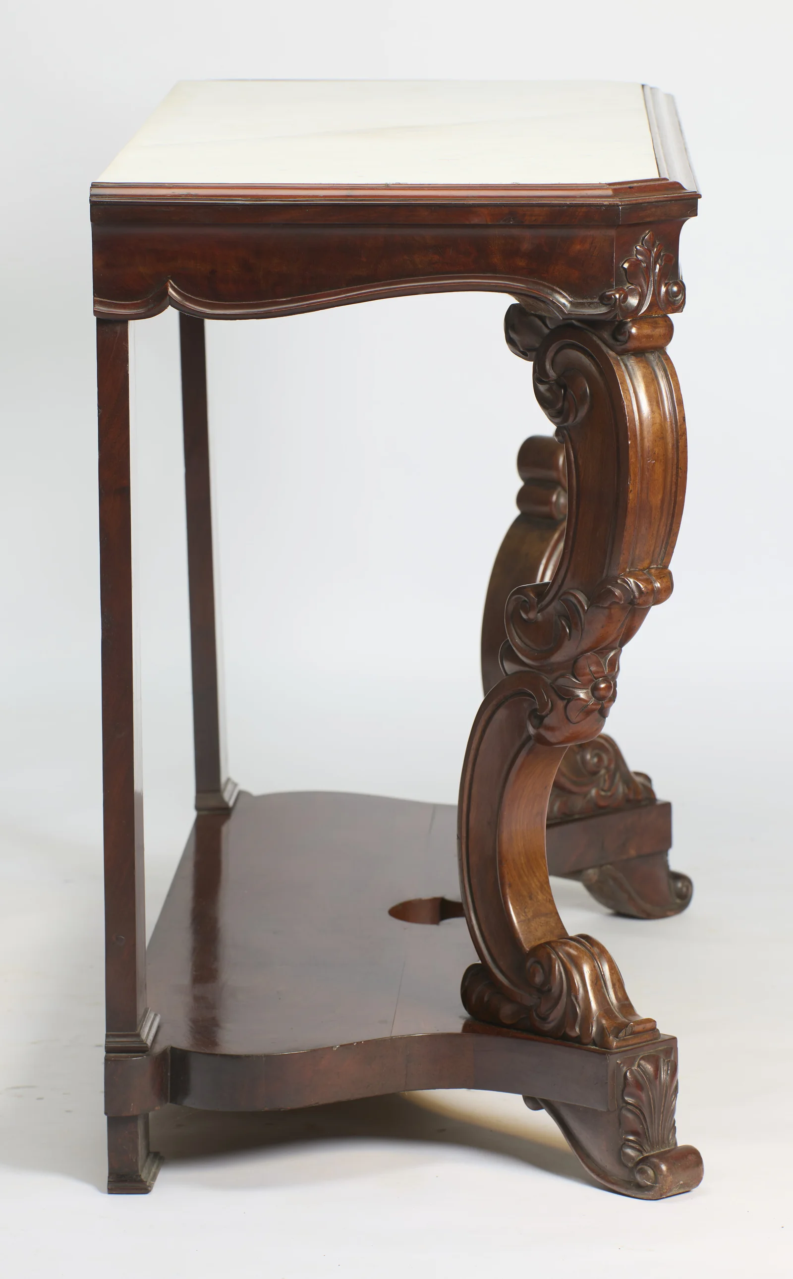 In profile the S-scroll support curves from the apron down to a leaf-carved foot, with the square rear pillar and the shaped undertier behind.