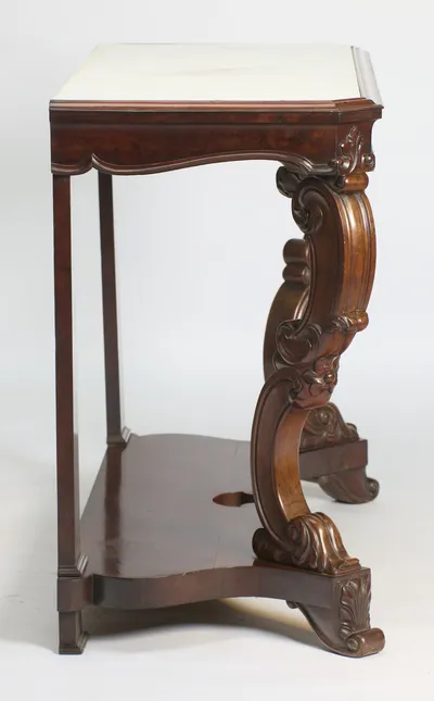 In profile the S-scroll support curves from the apron down to a leaf-carved foot, with the square rear pillar and the shaped undertier behind.