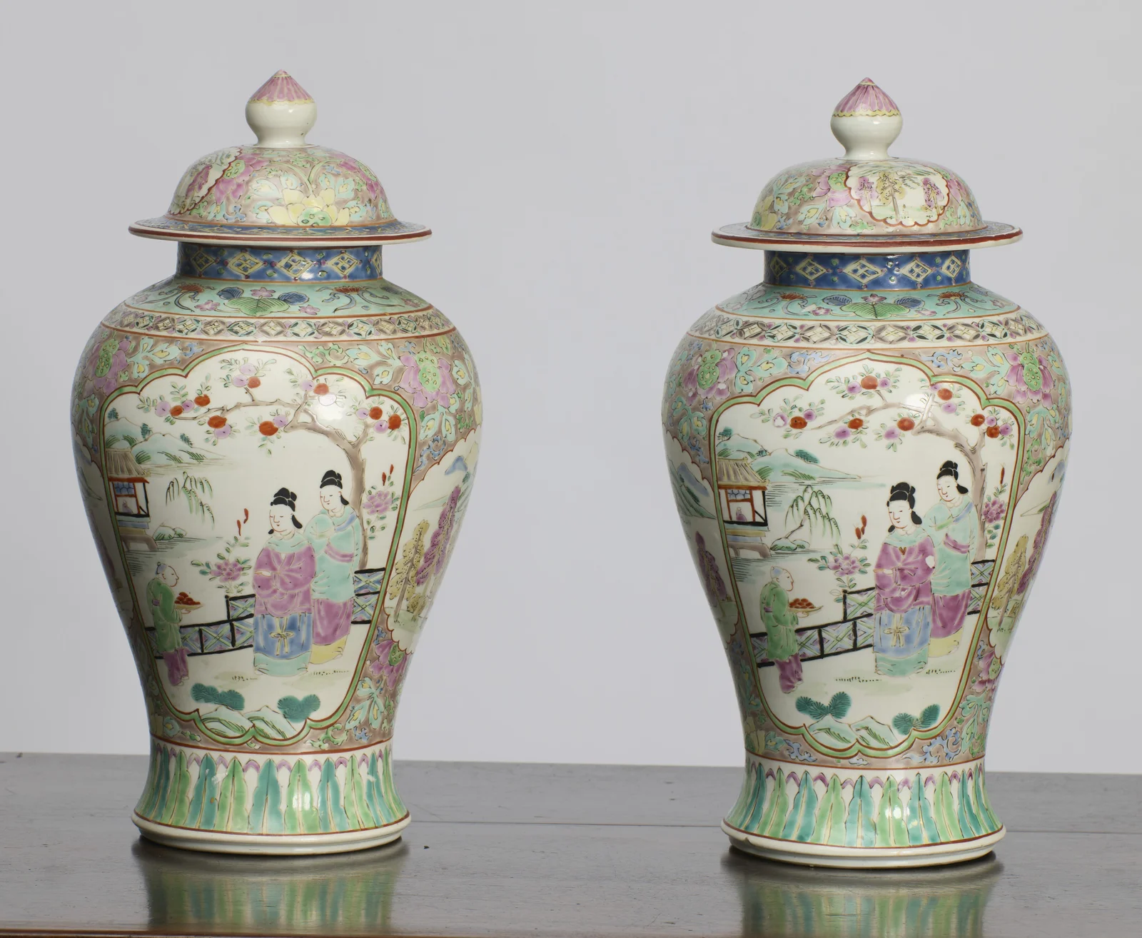 A closer angled view of the garden scenes, showing the domed covers with bud finials, the blue diaper collars and the flowering scroll ground flanking each panel.