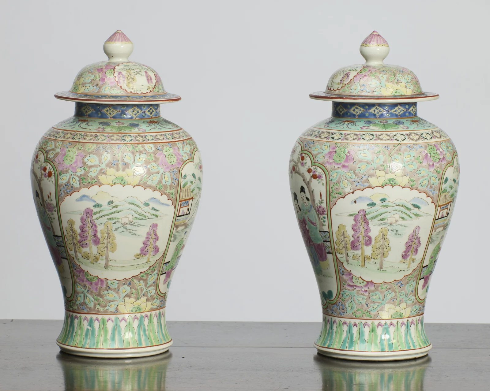 Each vase turned to the lobed oval panel painted with a river landscape of distant hills, sailing boats and pink and yellow trees, framed by dense flower and leaf scrolls.
