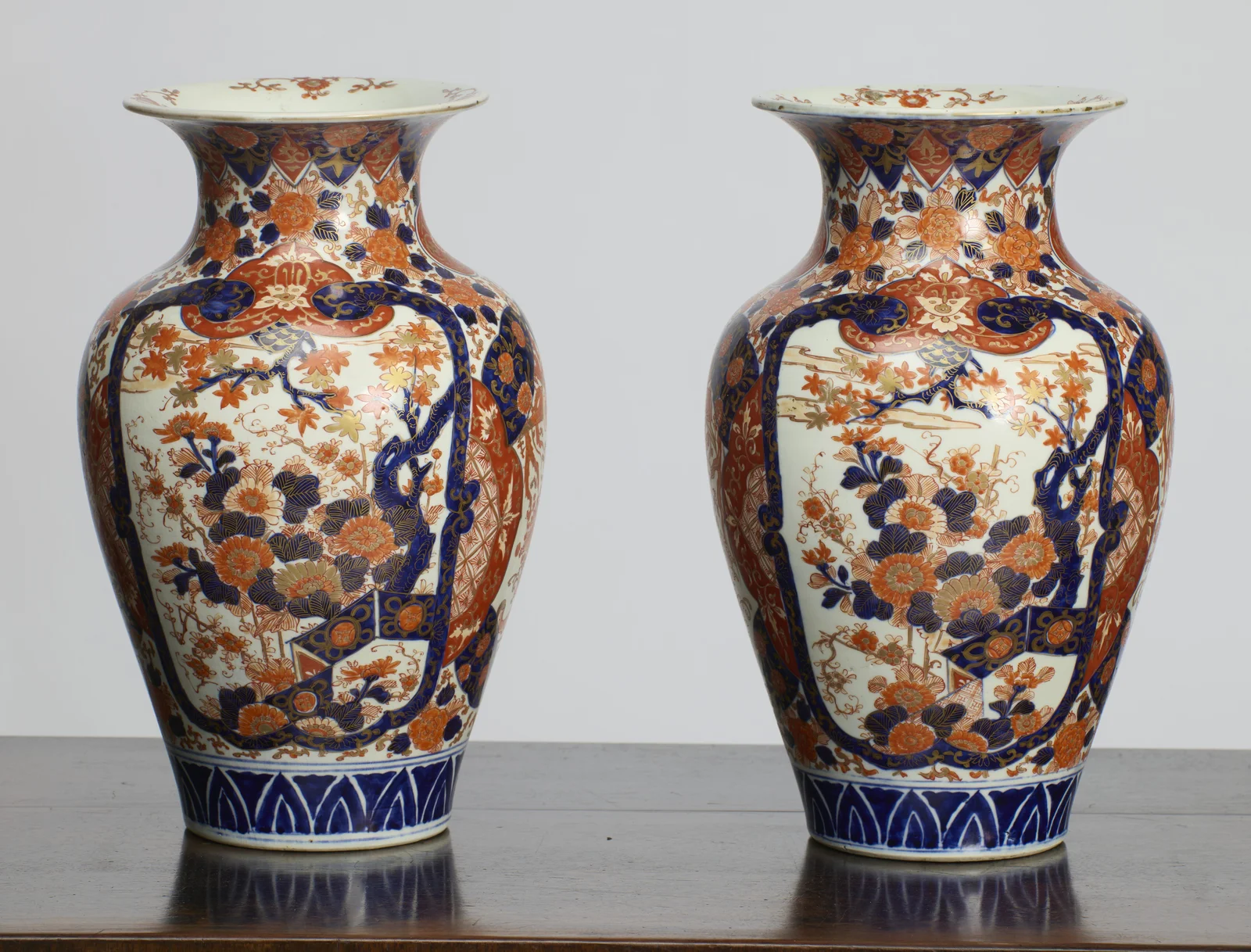 Both vases showing the large shaped panels painted with a flowering tree and massed blossom in blue, iron-red and gilt, above a band of blue stiff leaves at the foot.