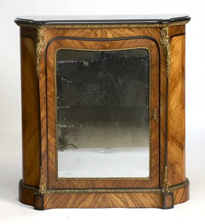 A level view of the front, the ebonised panel line sweeping around the arched mirror-glazed door between gilt foliate clasps.