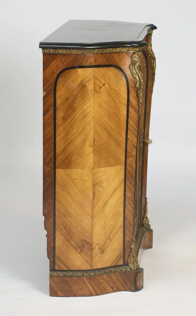 Quarter-matched veneer inside a shaped ebonised-line border, with the egg-and-dart gilt band running along the plinth.