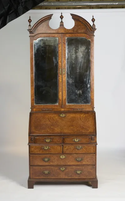 The bookcase complete: broken-arch pediment with three turned finials, arched mirror-glazed doors, sloped fall, and four short and two long drawers on bracket feet.