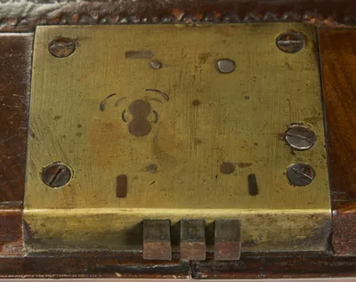 The gilt-metal lock plate on the inside edge of the fall, beside the tooled border of the writing surface.