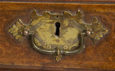 Engraved gilt-metal plate handle with shaped bail and keyhole, mounted on a feather-banded burr drawer front.