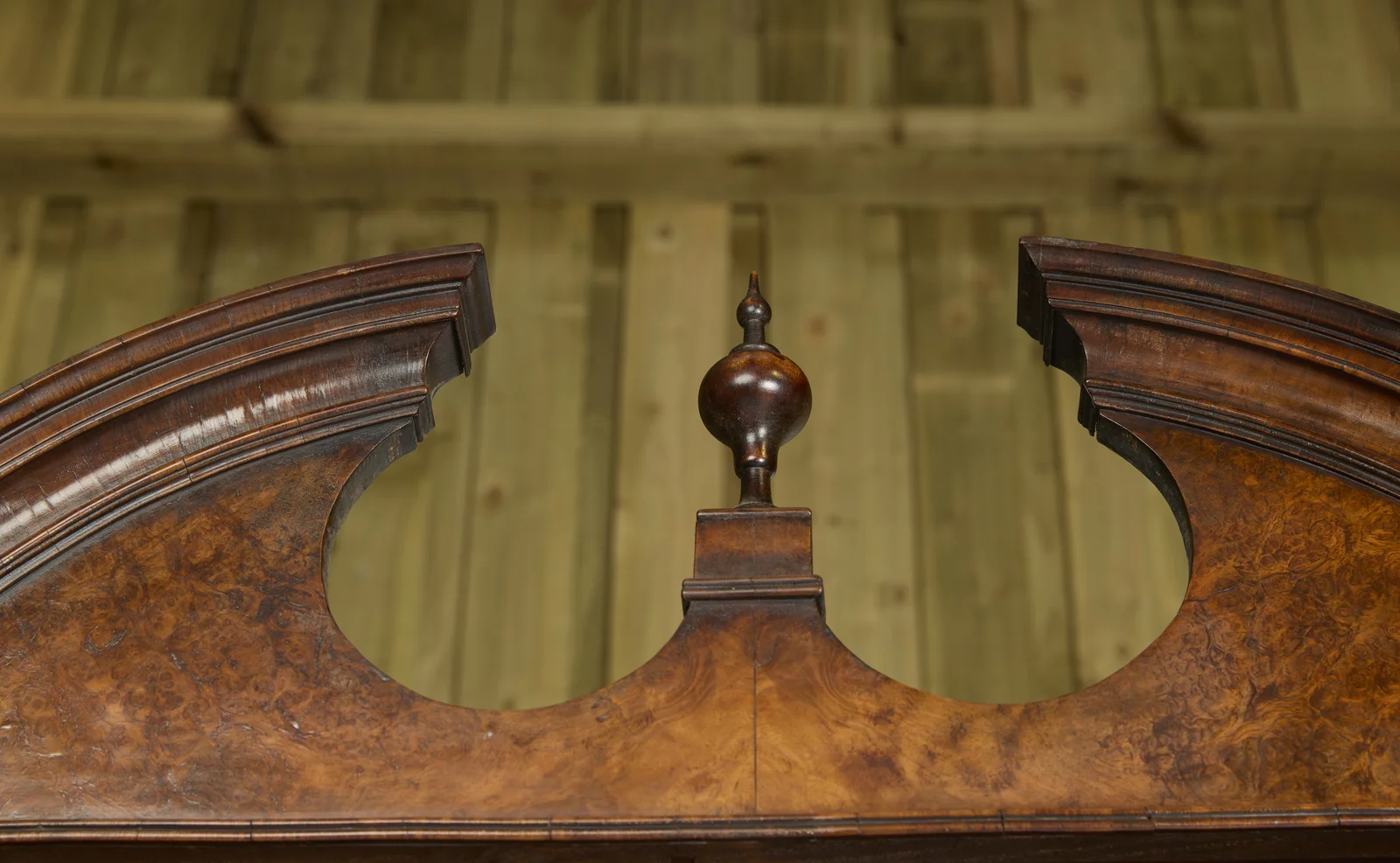 The broken arch meets a moulded plinth and turned finial at the centre, the whole face in tight burr figure.
