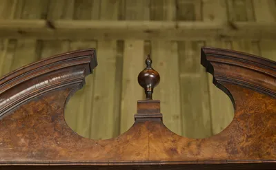 The broken arch meets a moulded plinth and turned finial at the centre, the whole face in tight burr figure.