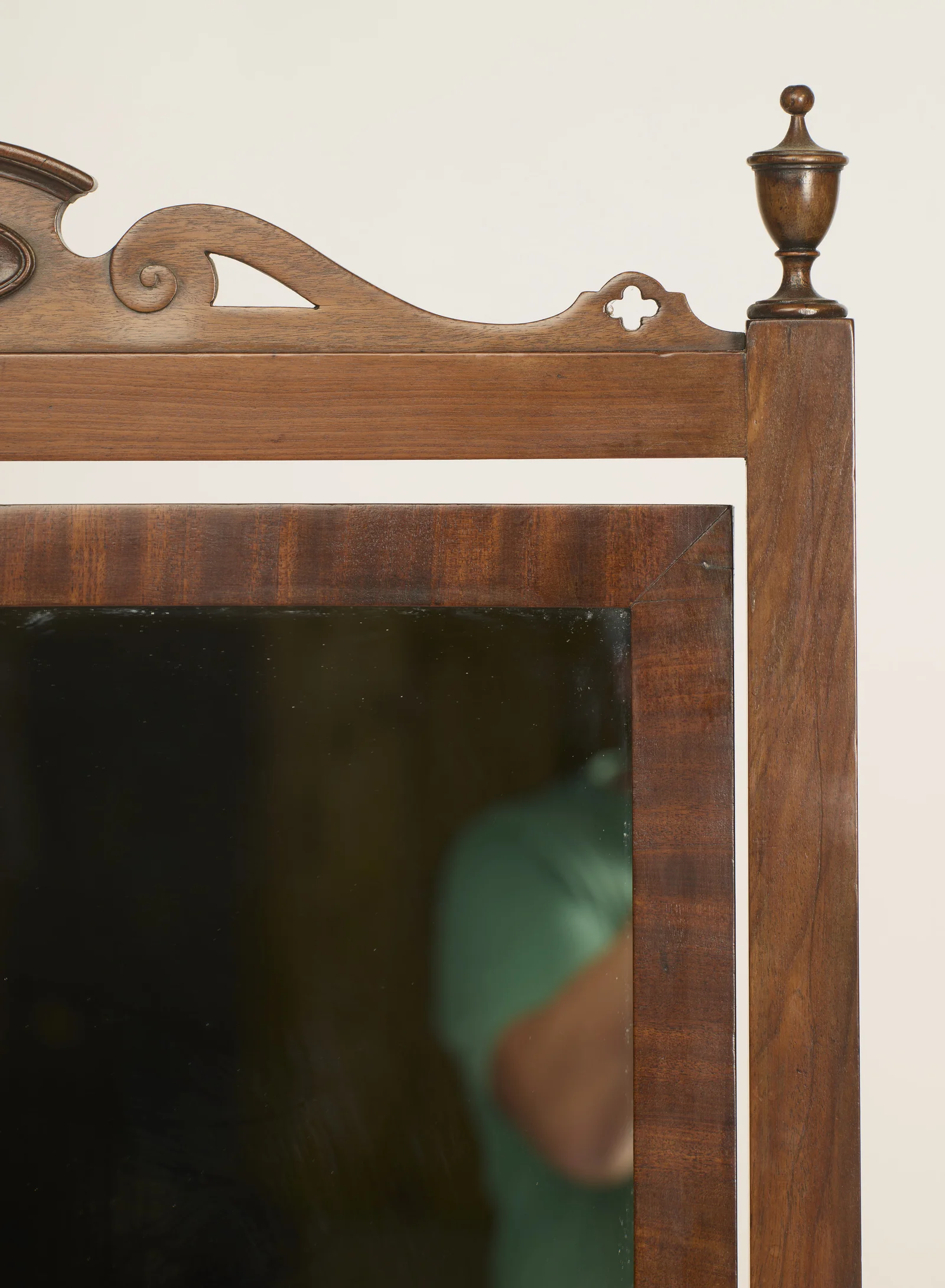 A turned urn finial caps the square upright, beside pierced scroll and quatrefoil cut-outs in the cresting above the crossbanded corner of the plate frame.