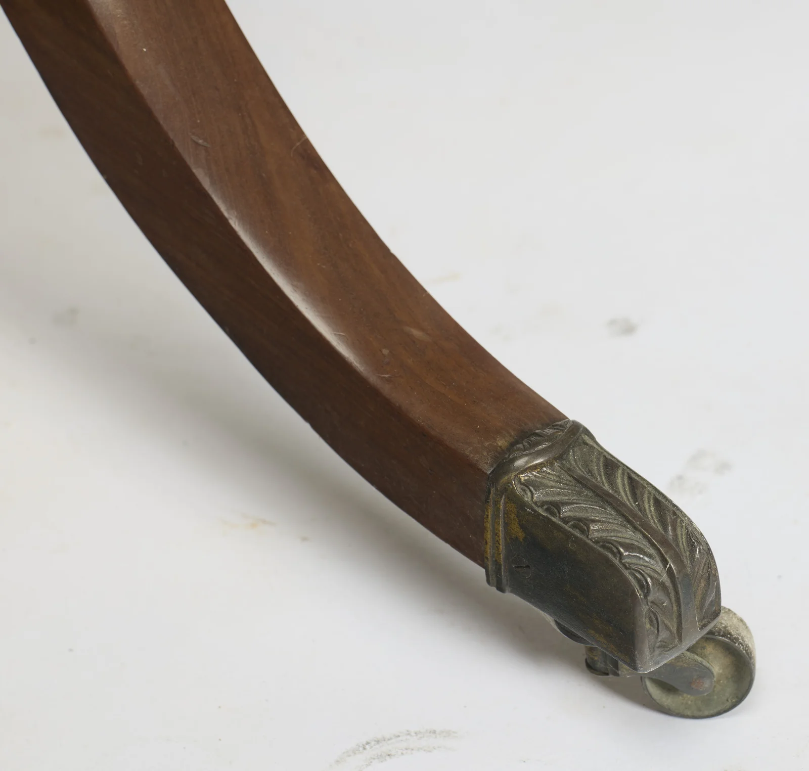 Close view of one leaf-cast metal cap, rubbed bright on the high spots of the casting, with its small roller wheel beneath.