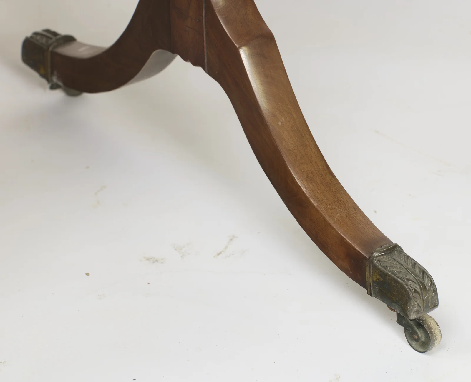 The leg sweeps down from its hipped shoulder to a leaf-cast metal cap and small roller wheel, the companion castor visible beyond.