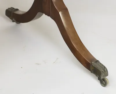 The leg sweeps down from its hipped shoulder to a leaf-cast metal cap and small roller wheel, the companion castor visible beyond.