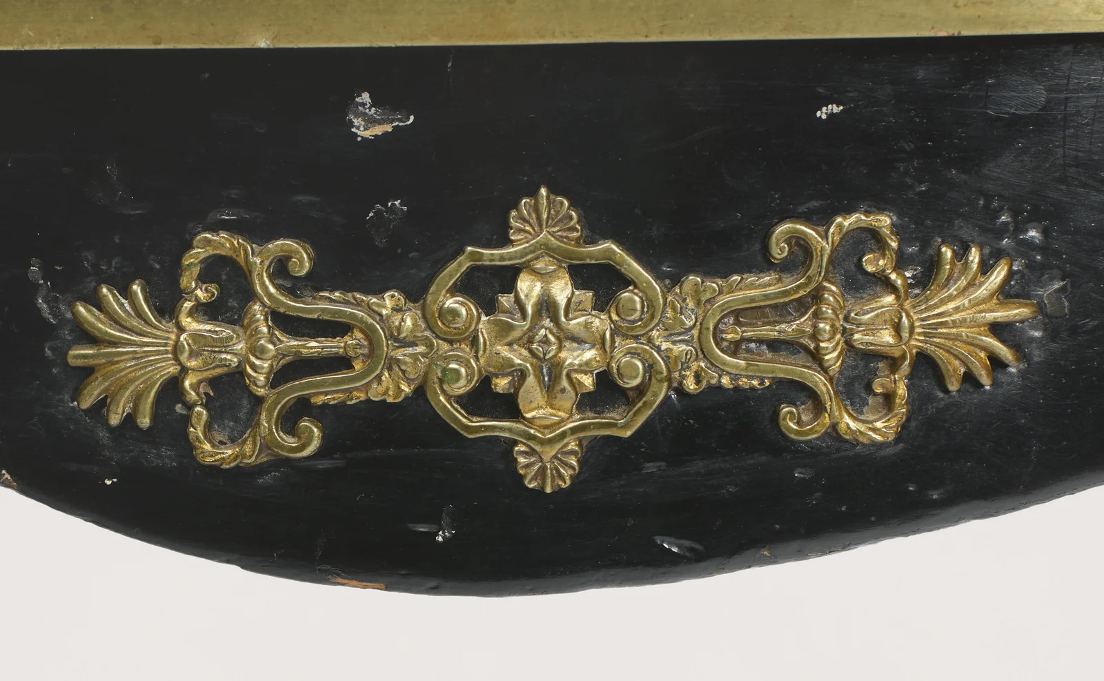 A gilt-metal mount of scrolls and fronds centred on the serpentine apron, beneath the screw-fixed brass band edging the top.