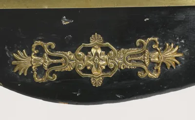 A gilt-metal mount of scrolls and fronds centred on the serpentine apron, beneath the screw-fixed brass band edging the top.