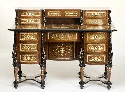 The desk complete: a raised superstructure of small bow-fronted drawers above a frieze drawer and two pedestals of three drawers each, every surface carrying pale engraved inlay within ebonised mouldings, on inlaid tapering legs joined by shaped stre