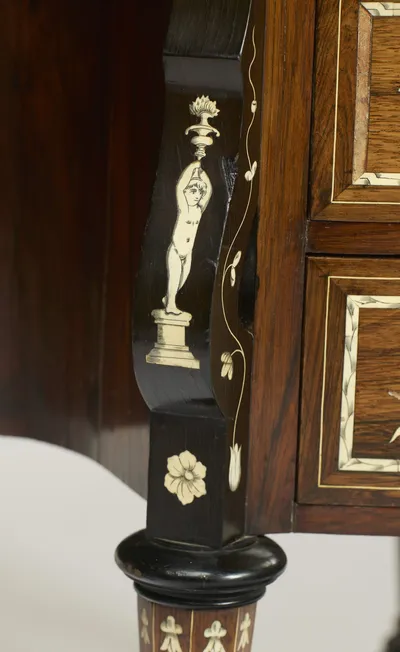 An engraved standing figure raising a flaming urn overhead, set on a plinth on the ebonised scroll support, with a trailing flowering stem beside and the inlaid leg below.