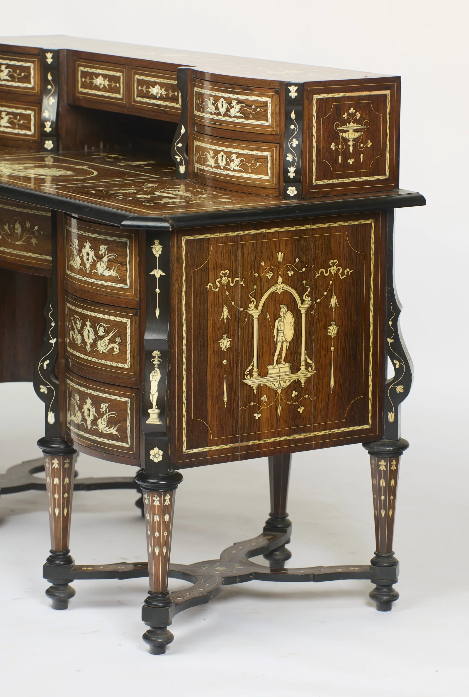 The drawer-box end inlaid with a pedestal urn, its ebonised scroll supports trailing flowering vines, above the pedestal drawers and their winged-dragon panels.