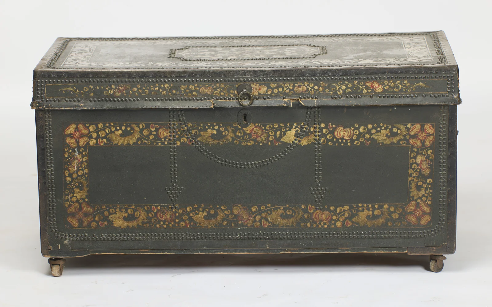 Swagged rows of domed studs around an oval keyhole escutcheon and ring pull, inside a painted flower border; small losses to the leather show along the lower edge of the lid.