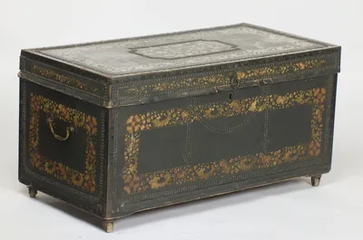 The hinged top and studded front seen together with the near end, its swan-neck handle hanging within a painted border of flowers and gilt foliage.