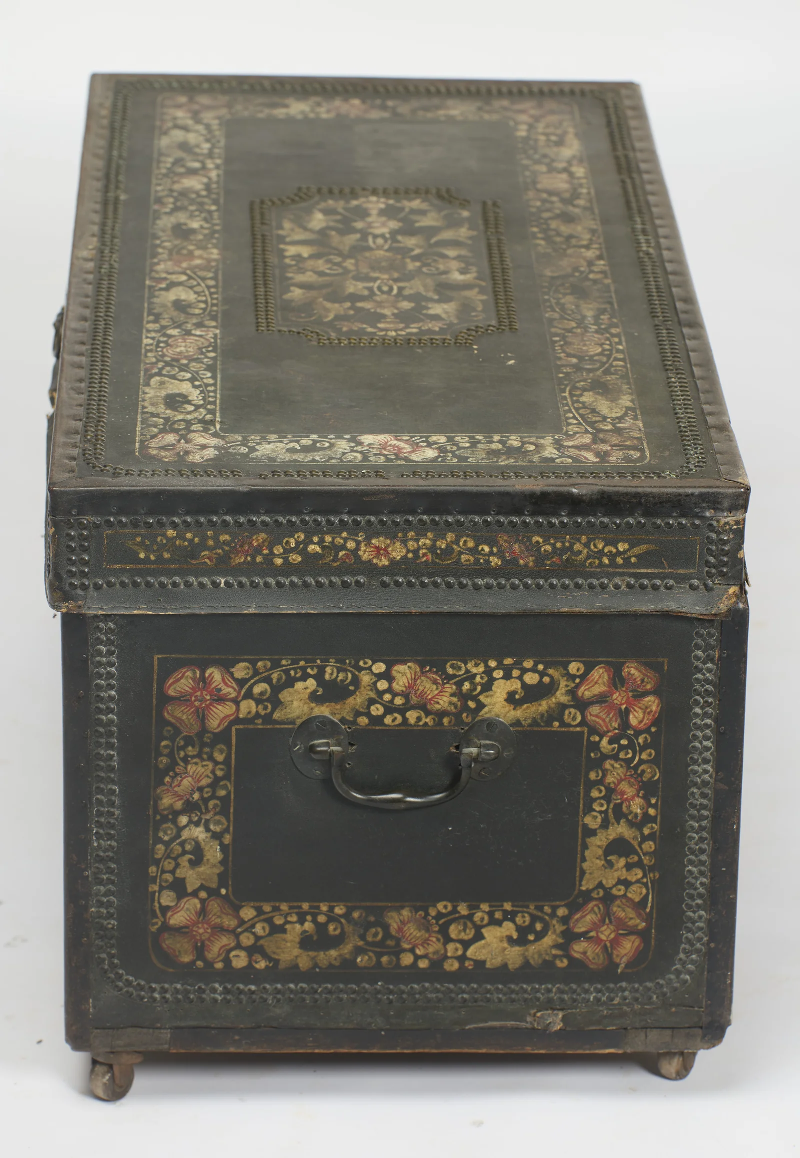 The full run of the top, its central stud-bordered cartouche enclosing painted foliage, above the end panel and its handle.