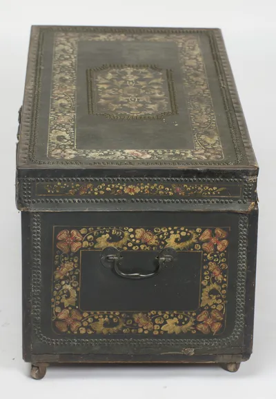 The full run of the top, its central stud-bordered cartouche enclosing painted foliage, above the end panel and its handle.