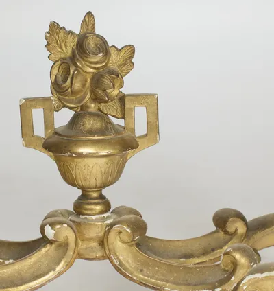 A two-handled urn carved with a band of leaves, roses spilling from its cover, raised at the crossing of the stretcher.