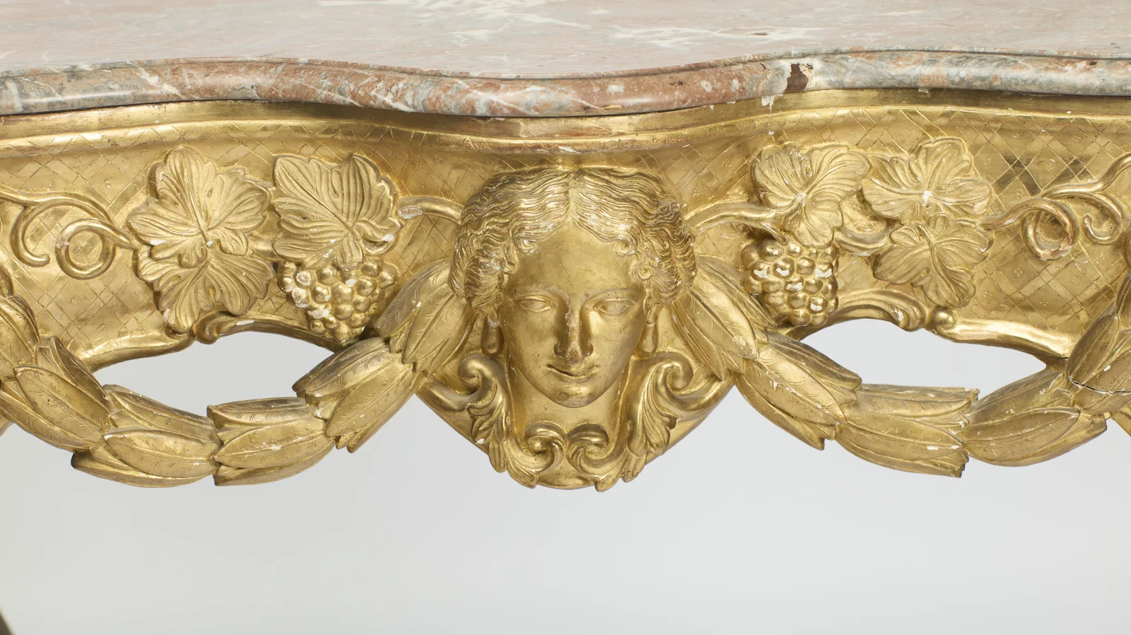 The mask anchors both husk swags, which loop through pierced openings in the apron beneath trailing vines.