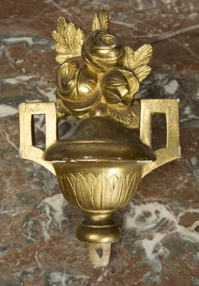 The urn lifts free of its socket, showing a bare dowel beneath the foot and handwritten script on each squared handle.