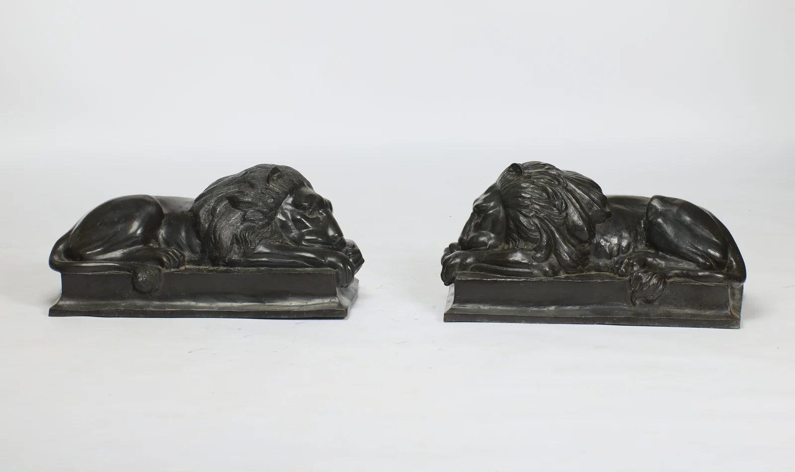 The lions at full length in profile, the tails dropping over the plinth edges to tufted tips.