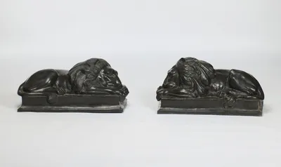 The lions at full length in profile, the tails dropping over the plinth edges to tufted tips.