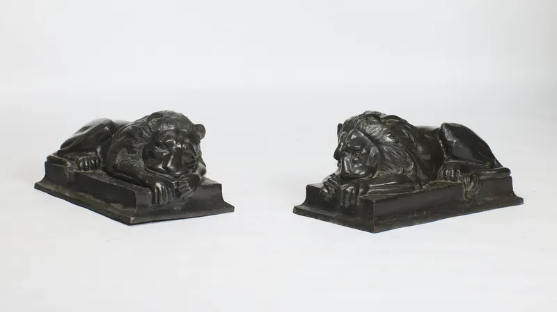 Pair of dark-patinated sleeping lions on stepped plinths