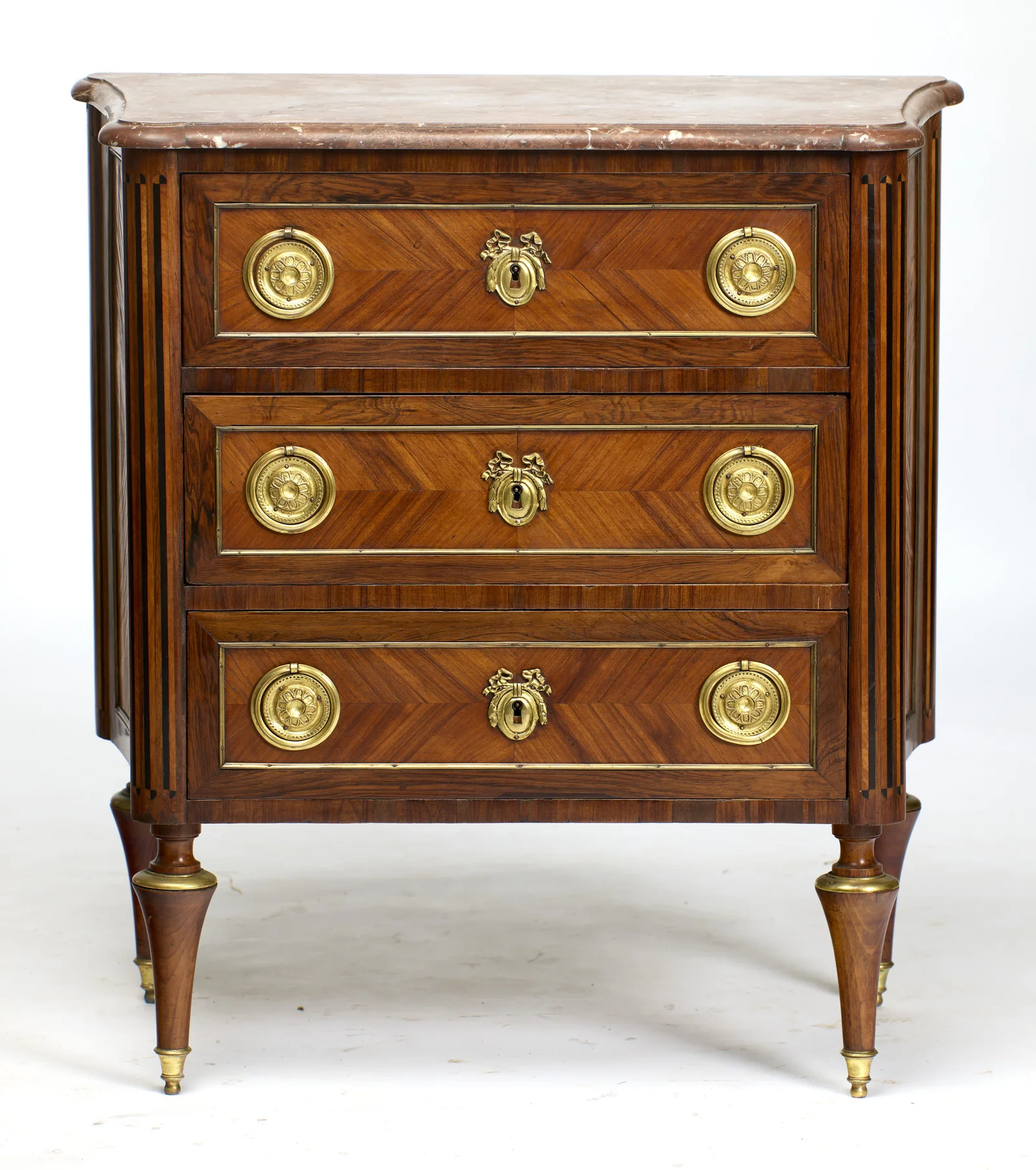 Three long drawers, each with a pair of pressed rosette ring handles and a ribbon-crested escutcheon, framed in beaded gilt-metal beneath the moulded marble top.