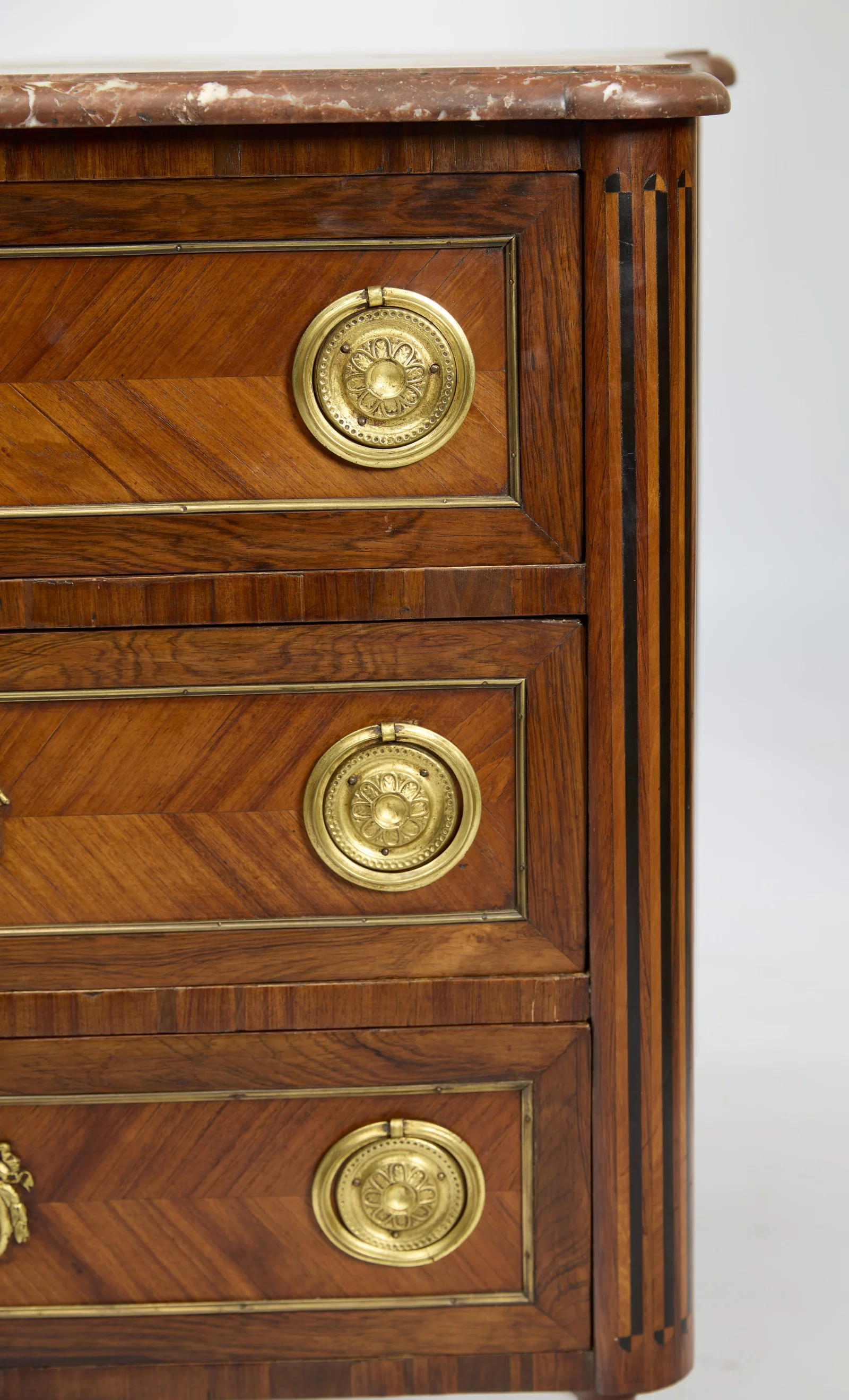 Three rosette ring handles descend beside the fluted canted corner, each drawer front framed by a fine gilt-metal moulding.
