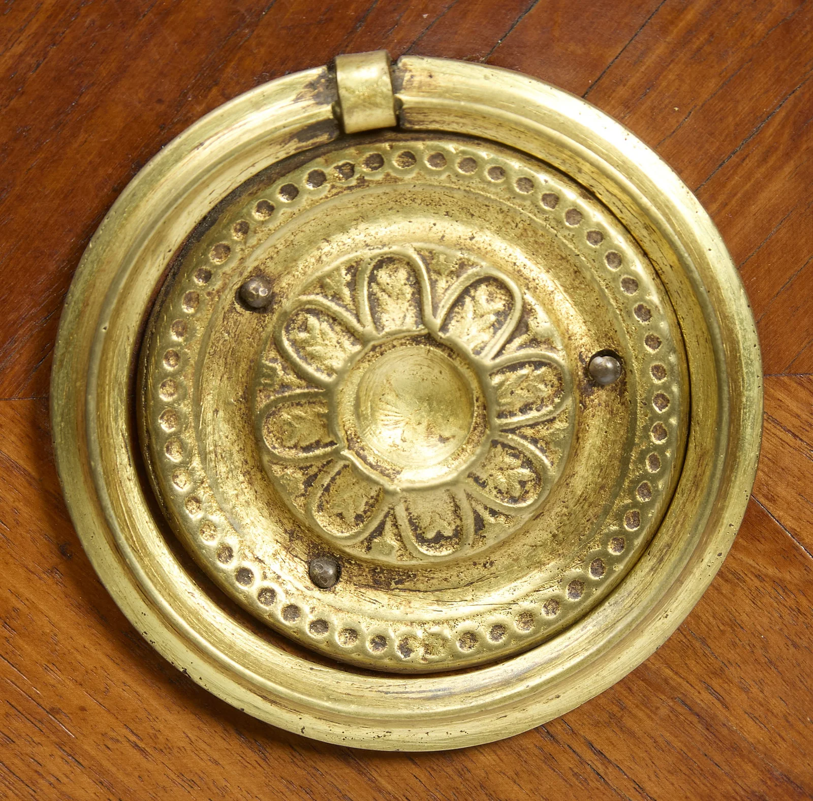 A pressed gilt-metal rosette within a beaded surround, its hinged ring hanging from the top mount; the corner flutes run behind.