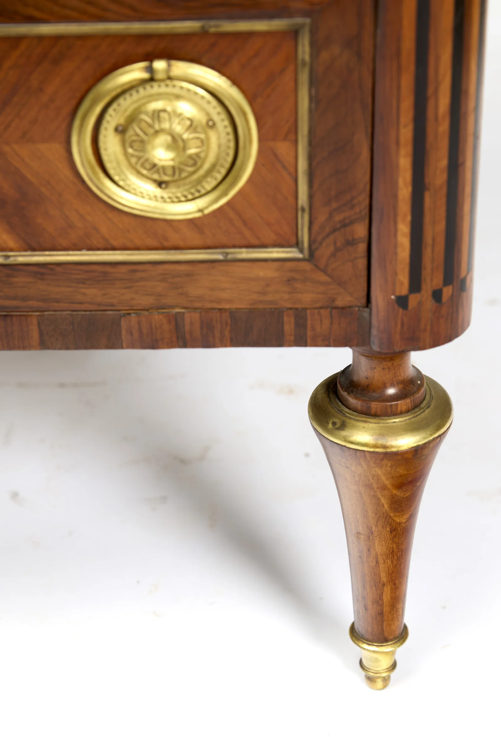 The turned tapering leg with a gilt-metal cup at its head and a matching ferrule and small ball at the toe, beneath the crossbanded frieze.