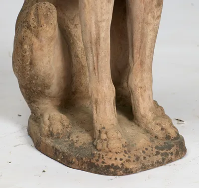 Knuckled paws rest on the rough oval base, its edge spotted dark with weathering.