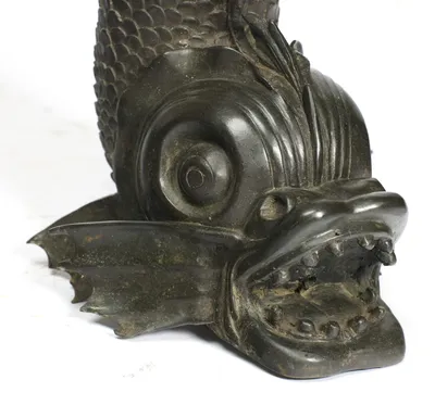The eye is cast within a spiralled volute above a gaping mouth set with rounded teeth, the webbed fin behind carrying pale green deposits.